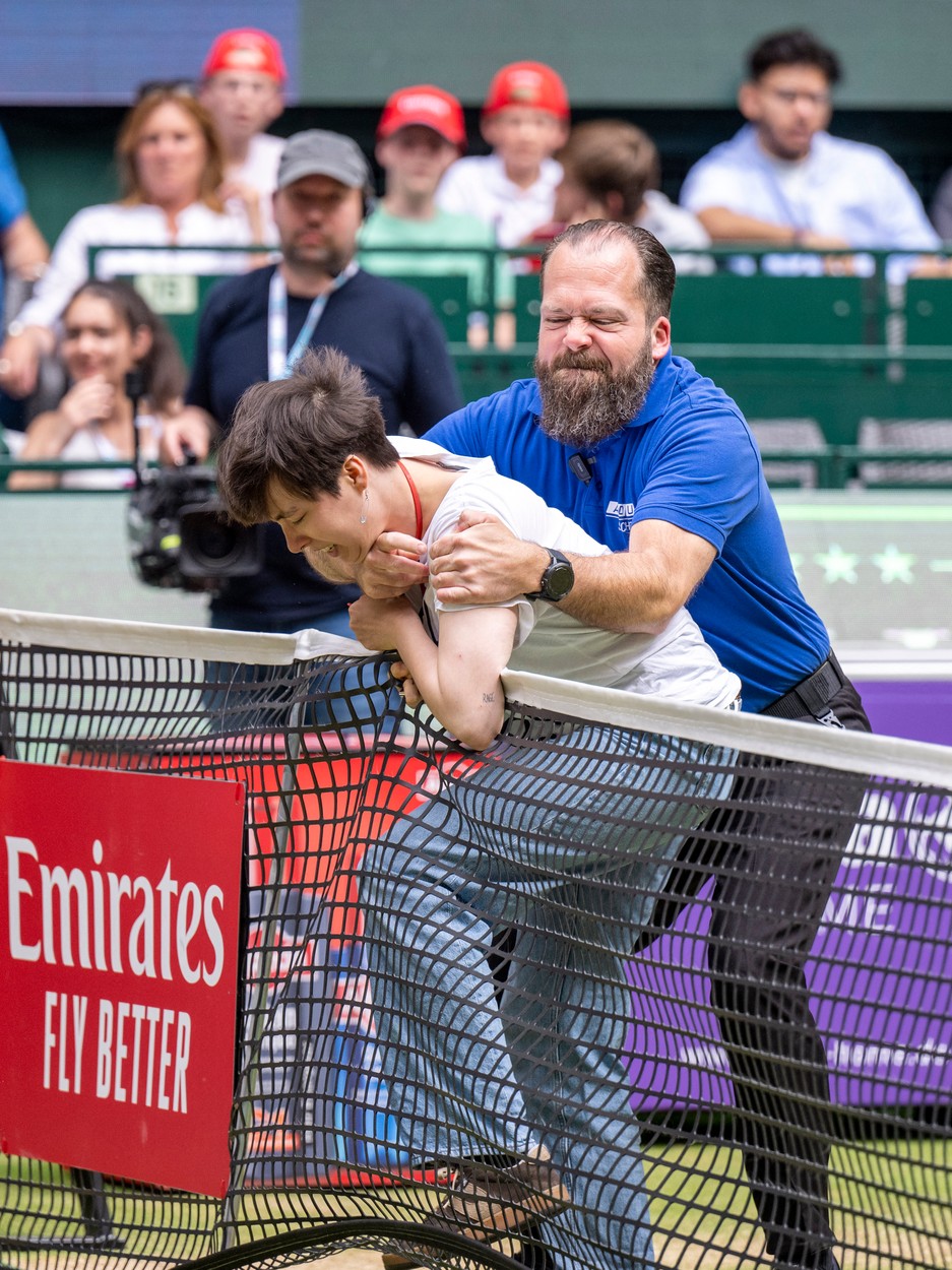 19 June 2022, North Rhine-Westphalia, Halle (westfalen): Tennis, ATP Tour, Singles, Men, Final, Medvedev (Russia) - Hurkacz (Poland): A woman tries to tie her neck to the net using a cable tie and is held down by a security guard. The woman is said to be a climate activist and has the text 