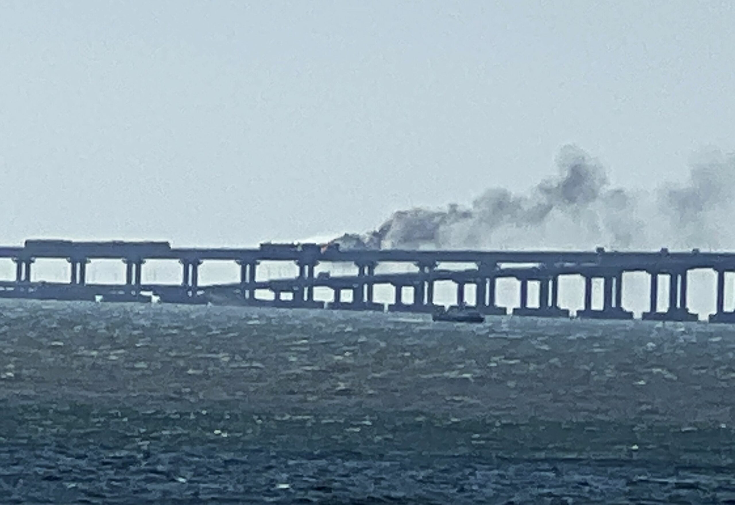8291779 08.10.2022 A view shows a smoke rising from a fire on Crimean Bridge connecting Russian mainland and Crimean peninsula over the Kerch Strait, in Crimea, Russia. Russia's National Antiterrorism Committee (NAC) said on Saturday that a truck was blown up on the Crimean Bridge, which caused an inflammation of seven fuel tanks of a railway train and a partial collapse of two car spans. The traffic and movement of trains across the Kerch Strait was temporarily suspended. The movement of ships in the Kerch Strait did not stop despite a fire on the bridge. Elena Ivanova / Sputnik