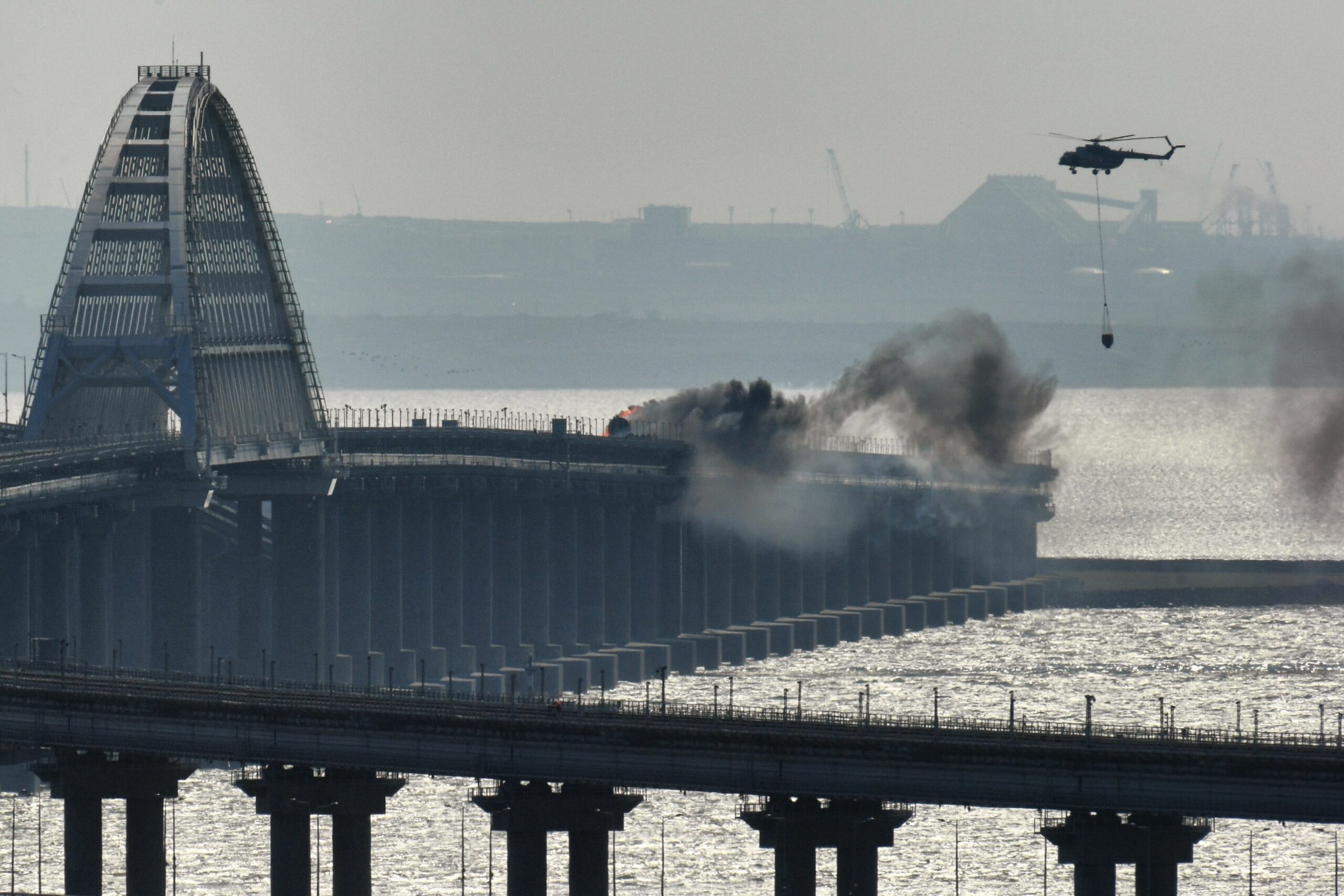 8291785 08.10.2022 A helicopter drops water to stop fire on Crimean Bridge connecting Russian mainland and Crimean peninsula over the Kerch Strait, in Crimea, Russia. Russia's National Antiterrorism Committee (NAC) said on Saturday that a truck was blown up on the Crimean Bridge, which caused an inflammation of seven fuel tanks of a railway train and a partial collapse of two car spans. The traffic and movement of trains across the Kerch Strait was temporarily suspended. The movement of ships in the Kerch Strait did not stop despite a fire on the bridge. Konstantin Mihalchevskiy / Sputnik