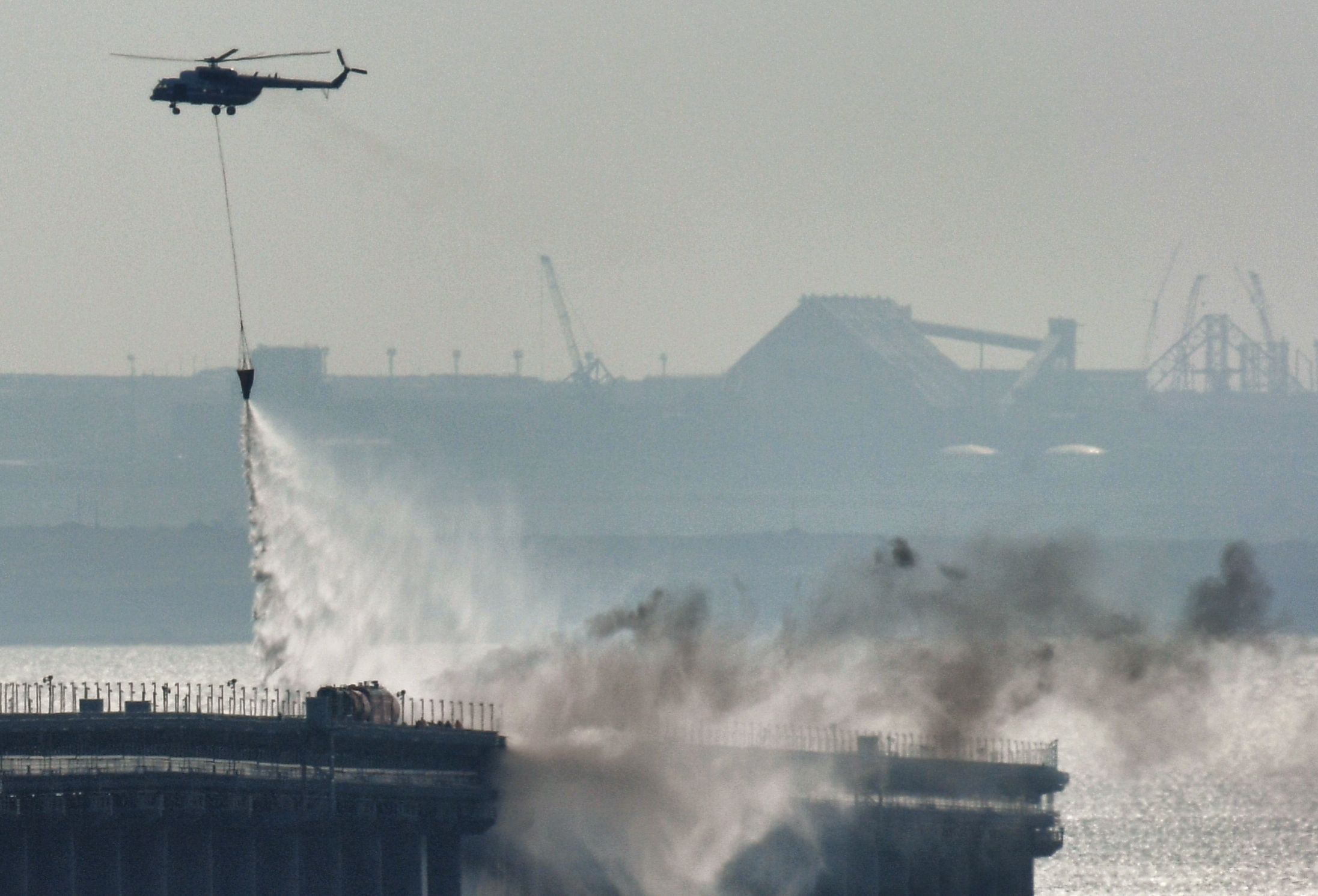 8291789 08.10.2022 A helicopter drops water to stop fire on Crimean Bridge connecting Russian mainland and Crimean peninsula over the Kerch Strait, in Crimea, Russia. Russia's National Antiterrorism Committee (NAC) said on Saturday that a truck was blown up on the Crimean Bridge, which caused an inflammation of seven fuel tanks of a railway train and a partial collapse of two car spans. The traffic and movement of trains across the Kerch Strait was temporarily suspended. The movement of ships in the Kerch Strait did not stop despite a fire on the bridge. Konstantin Mihalchevskiy / Sputnik