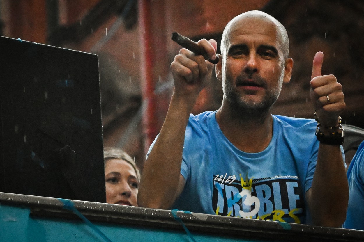 Manchester City's Spanish manager Pep Guardiola smokes a cigar as he clebrates with his players during an open-top bus victory parade in the streets of Manchester, northern England on June 12, 2023, as they celebrate with the European Cup, the FA Cup and the Premier League trophies. Manchester City tasted Champions League glory at last on Saturday as a second-half Rodri strike gave the favourites a 1-0 victory over Inter Milan in a tense final, allowing Pep Guardiola's side to complete a remarkable treble. Having already claimed a fifth Premier League title in six seasons, and added the FA Cup, City are the first English club to win such a treble since Manchester United in 1999.,Image: 782976902, License: Rights-managed, Restrictions: , Model Release: no
