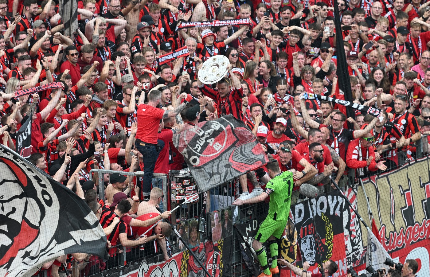 18 May 2024, North Rhine-Westphalia, Leverkusen: Soccer, Bundesliga, Bayer Leverkusen - FC Augsburg, Matchday 34, BayArena, The Leverkusen fans cheer with the championship trophy, which Leverkusen goalkeeper Lukas Hradecky (u) brought into the fan curve. IMPORTANT NOTE: In accordance with the regulations of the DFL German Football League and the DFB German Football Association, it is prohibited to exploit or have exploited photographs taken in the stadium and/or of the match in the form of sequential images and/or video-like photo series.,Image: 874180012, License: Rights-managed, Restrictions: , Model Release: no
